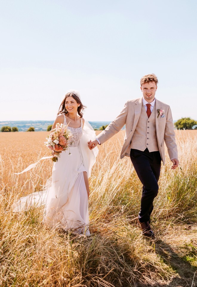 Relaxed bride and groom walking through the Cotswolds countryside, with natural daytime  wedding portraits