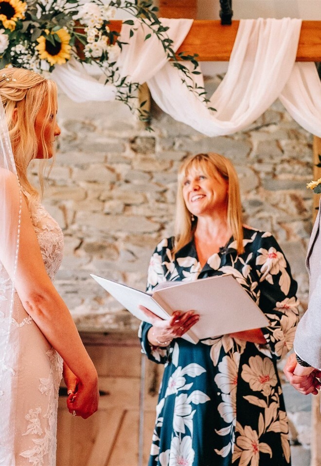 Celebrant reading to a couple underneath a wooden frame adorned in muslin and sunflowers