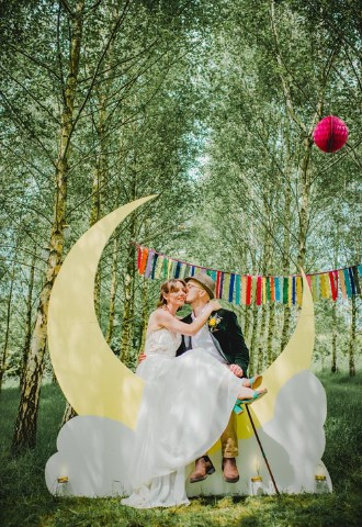 bride and groom sitting on crescent moon sculpture with bright ribbon background