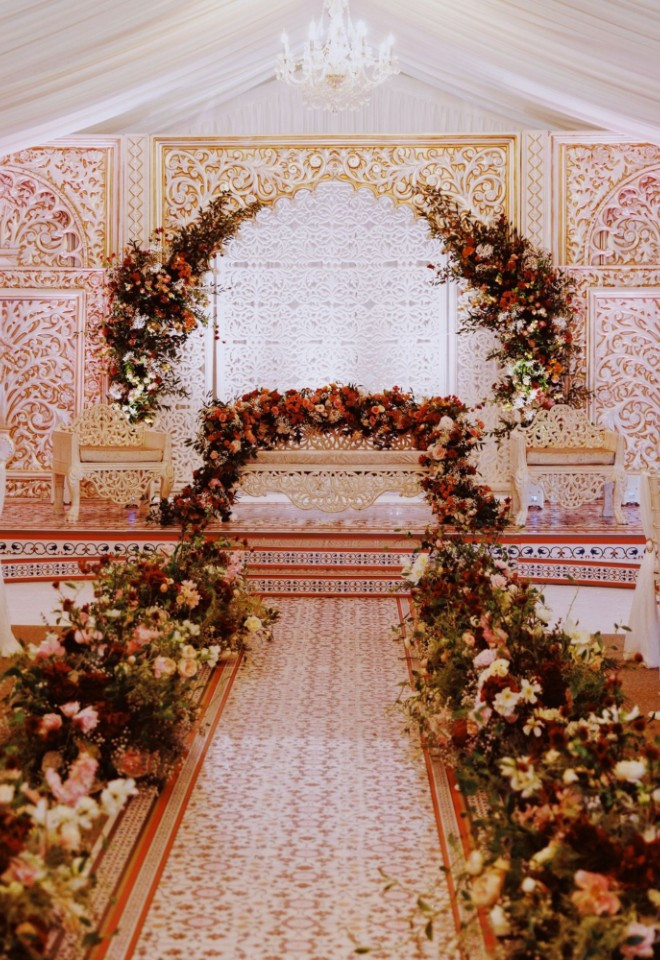 Intricate stage and reception setup inside the draped Pavilion marquee at North Mymms Park, featuring a decorated stage with carved backdrop panels, an arch of rich autumnal flowers, and a patterne