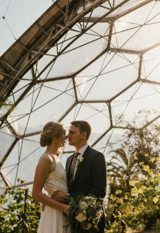 Couple beneath clear hexagonal ceiling of the Eden Project on wedding day