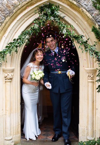 bride and groom exit their church ceremony through a flower and foliage arch made by ann laing flowers, harwell, oxfordshire