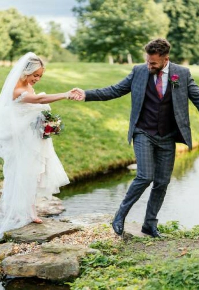 Groom guiding bride across the stones and waterfall outside- Sprowston Manor Norwich