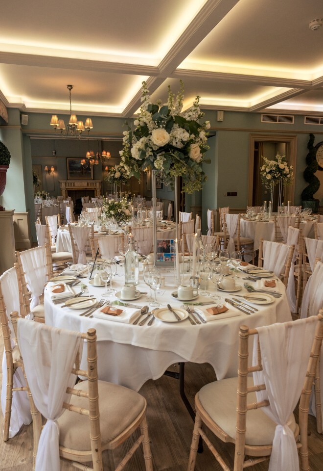 Wedding breakfast setup at Washingborough Hall Hotel with round tables dressed in white linens, elegant floral centrepieces, and softly lit chandeliers.