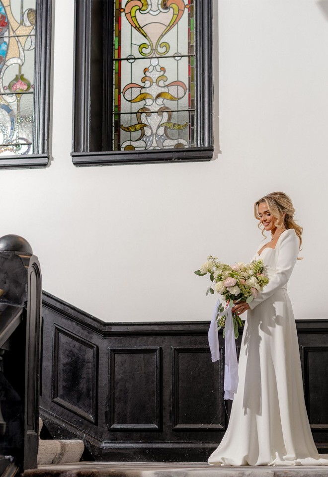 Bride on staircase beneath stained glass windows at The Collector’s Hall wedding venue in Glasgow
