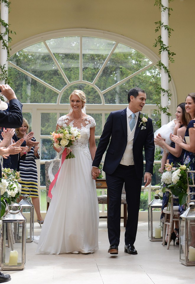 Leaving the orangery at Stapleford Park, a happy bride and groom smile at guests as they walk down the aisle hand in hand