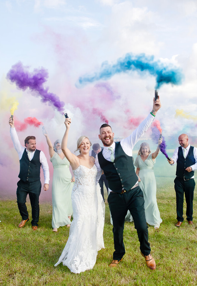 “Bride and groom celebrating with wedding party using colourful smoke bombs at Bowerchalke Barn Dorset”