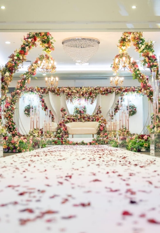 Step into elegance at The Willows. A breathtaking floral walkway leads to a romantic stage adorned with chandeliers and blooms — the perfect setting for an unforgettable wedding celebration.