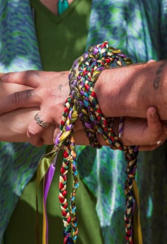 close up fo the couples arms tied togethre in a colourful dispay of cords in a unity knot