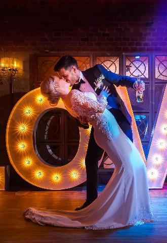 Groom kisses his bride in front of a love sign on the dance floor at their wedding reception