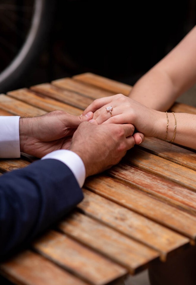 An engaged couple hold hands across an Oxford cafe table.