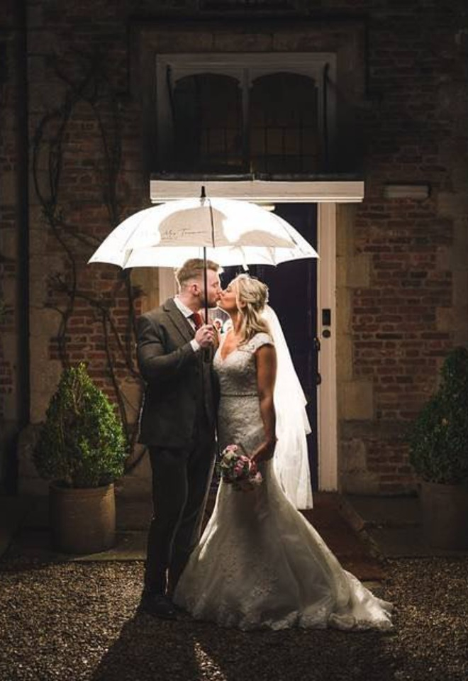Bride and groom stood underneath an umbrella illuminated outside of Hockwold Hall wedding venue