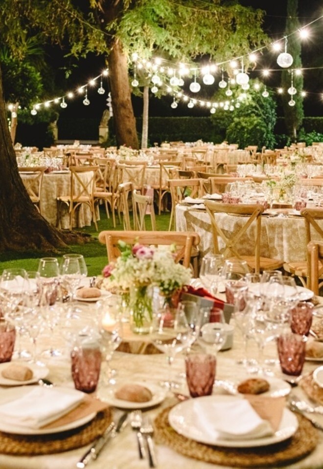 Circular tables amongst trees with warm colour scheme and fairy lights