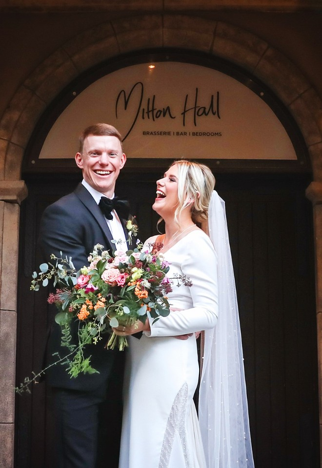 Mitton Hall wedding bride holding beautiful bouquet of flowers stood next to the groom in the main doorway