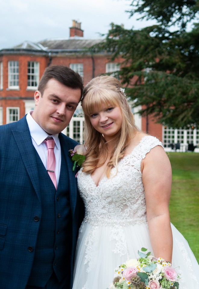 Newlywed couple smile to camera with their beautiful wedding venue in the background