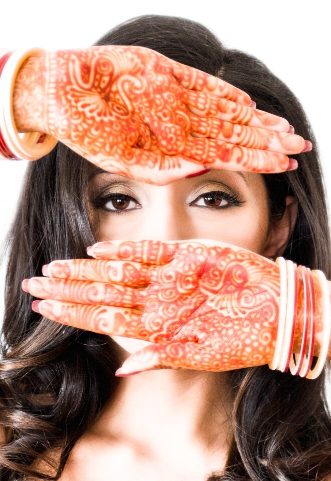 Wedding portrait of Indian bride looking through her two raised palms which show a henna design