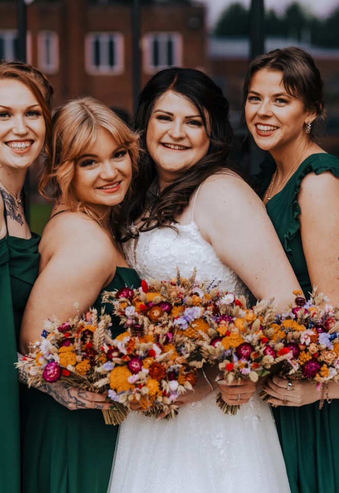 bride stood with bridesmaids in dark green dresses holding orange, red autumnal coloured bouquets