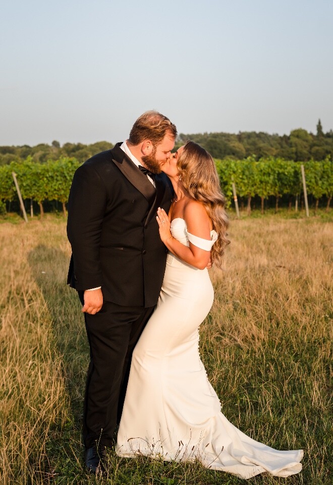 Bride and groom kissing in golden evening light in a vineyard during their wedding.