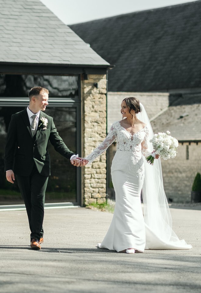 A bride and groom walking through the grounds and barn area at an exclusive Oxfordshire wedding venue
