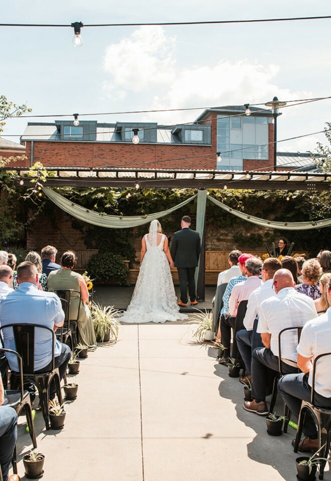 Courtyard ceremony with couple stood at the top of the aisle outside in sunny weather