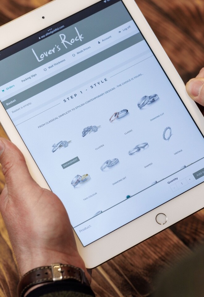 Someone holding an iPad with he Lovers Rock Diamonds ring builder tab of his website open