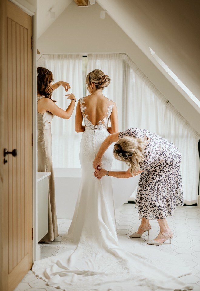 Mother and Bridesmaid help Bride get ready for wedding at Alfrison Gardens