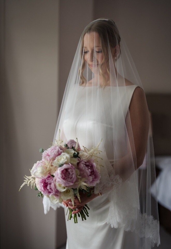 Bride holding her bouquet beneath her veil during bridal preparations.