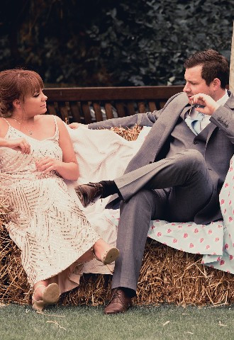 Wedding guests sit on straw bail sofa at country vintage wedding