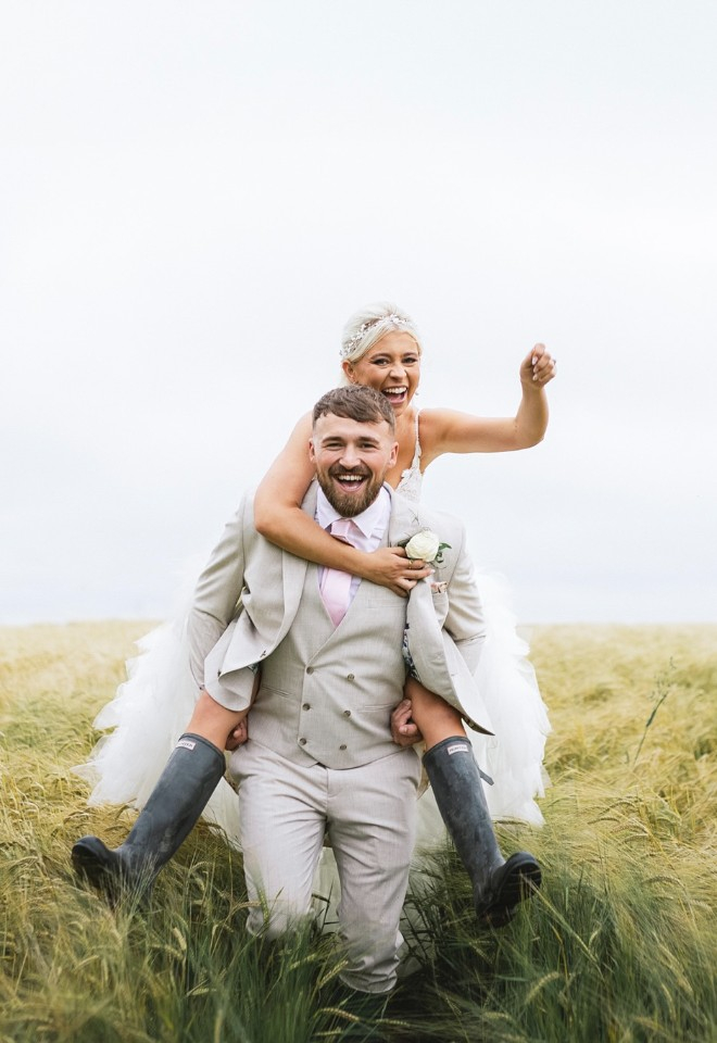 groom carrying the bride wearing wellies in the field of long grass at manor hill house in bromsgrove