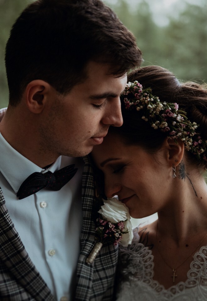 Bride and groom share a quiet, intimate moment by the water, with soft natural light and a romantic floral headpiece – documentary-style wedding photography.