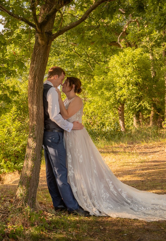 Bride and groom embrace in woodland beside the lake at Stoke Place in Buckinghamshire on a warm summer evening