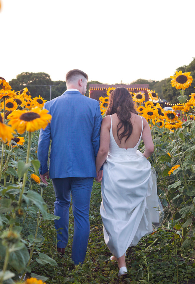 “Bride and groom walking through sunflower field at The Old Vicarage Dorset summer wedding”