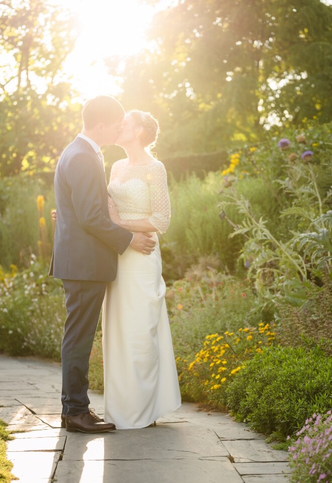 Backlit bride and groom kissing in a sunlit garden, captured by a Cotswolds and Bristol wedding photographer.