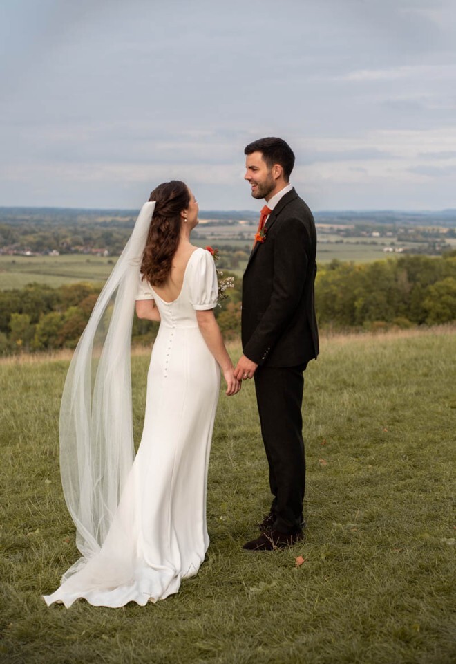 A newly married couple smile at each other at the top of Wittenham clumps.