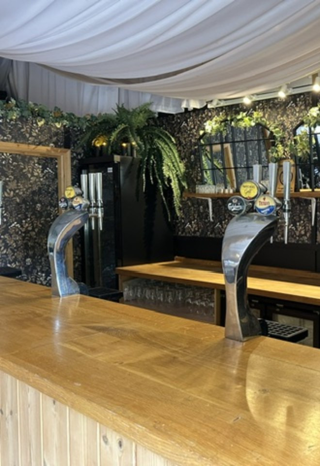 Wedding bar at Duvale Priory in Tiverton, Devon, featuring a rustic wooden counter, draught beer taps, botanical décor and elegant greenery.