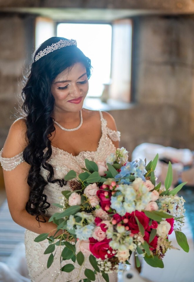 Bride holding colourful bridal bouquet in preparation room at coastal Cornwall wedding by FLOWERS BY ANYA