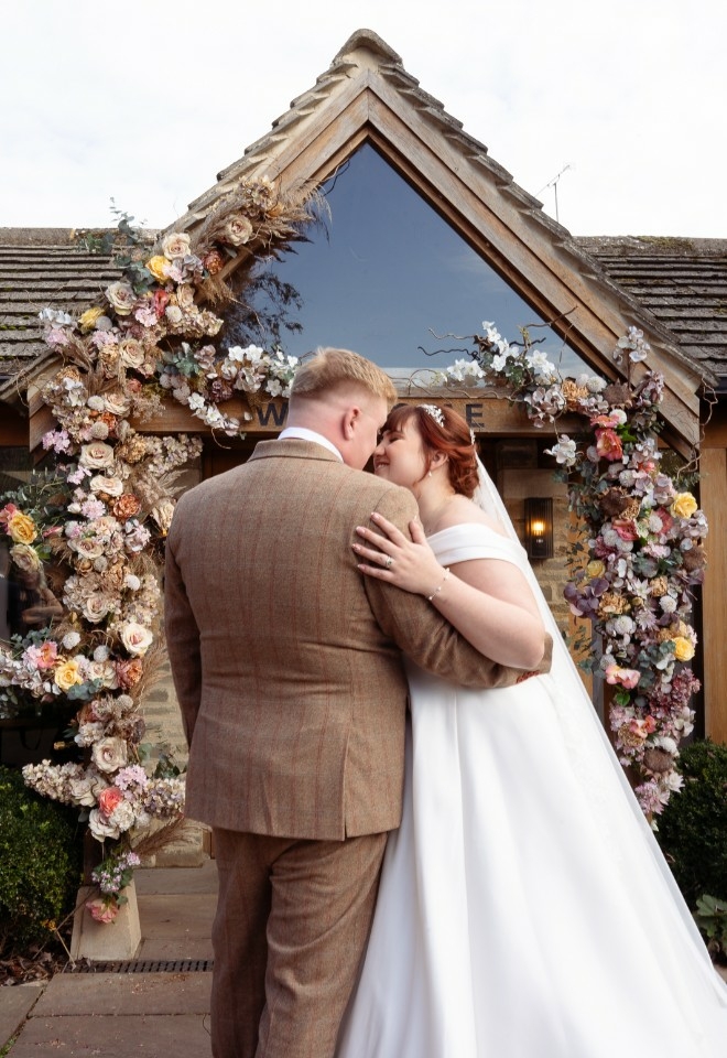 Bride and Groom embracing and about to kiss in front of their venue entrance covered in peach a lilac coloured flowers