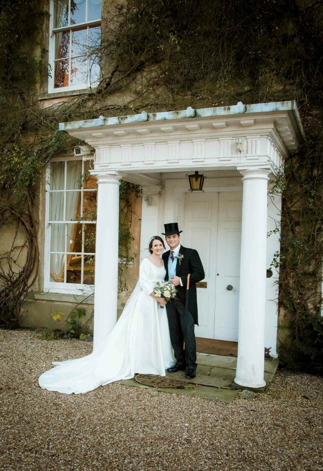 "Bride and groom in traditional wedding attire outside country house