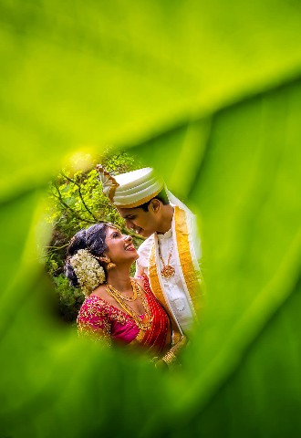Creative portrait of the bride and groom through a green leaf on their wedding day