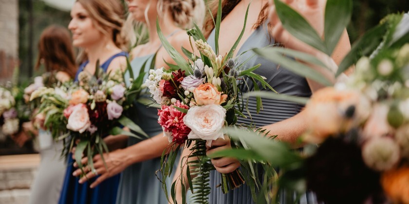 Bridesmaids standing outdoors holding mixed floral bouquets with greenery, wearing blue dresses during a wedding ceremony