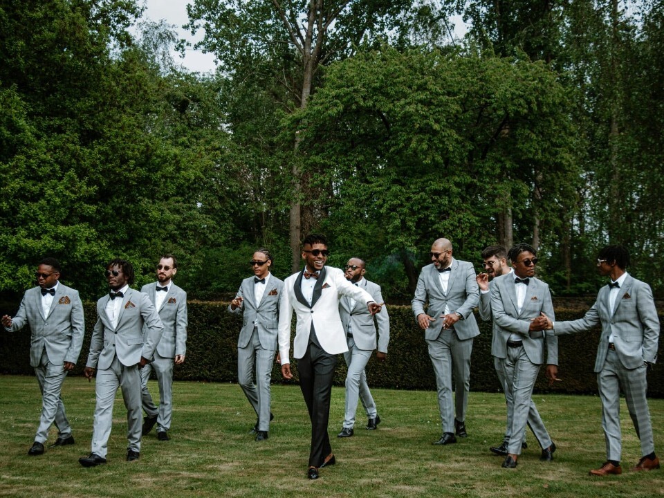 Groom and his entourage (including best man, ushers and groomsmen) walking towards wedding ceremony. They are smiling at each other.