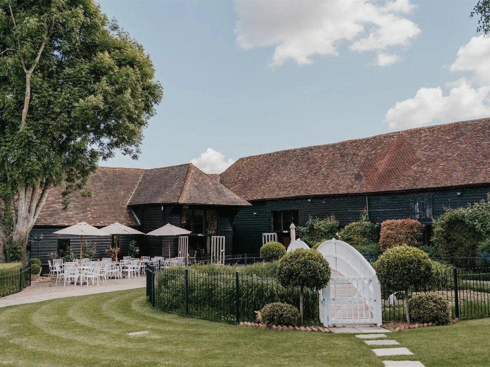 Winters Barn wedding venue in Kent with black timber barns, landscaped gardens and an outdoor courtyard set up with white tables and parasols.