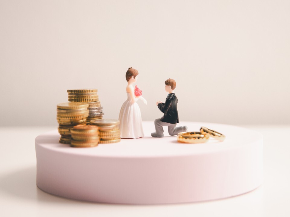 Models of a bride and groom next to coins and wedding rings