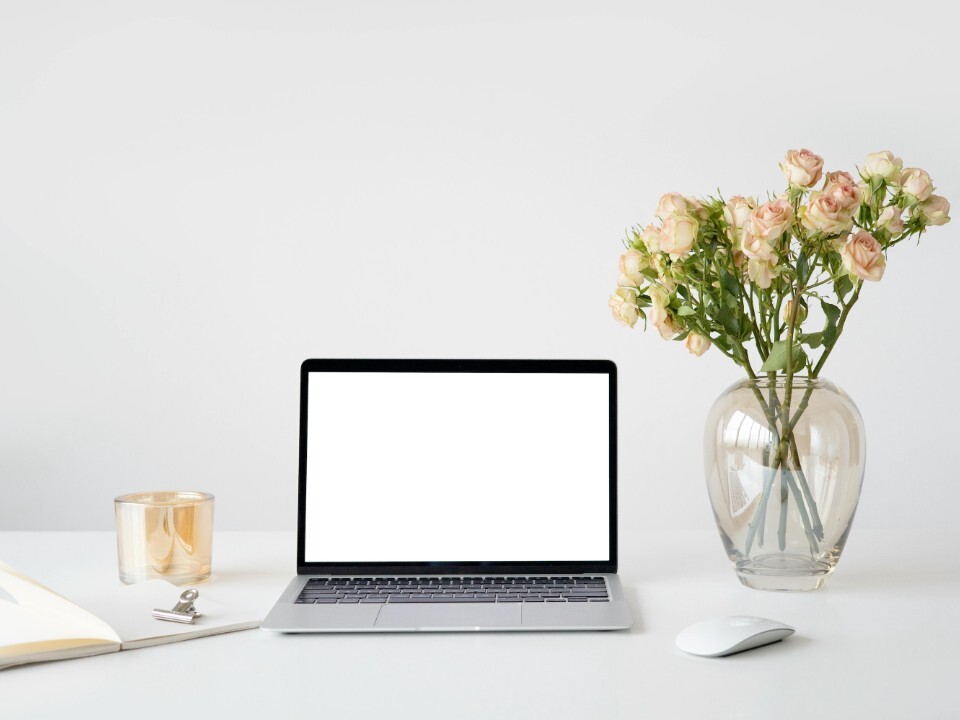 Laptop on desk with blank screen, notebook and roses, representing planning a wedding website at home.