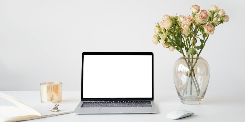 Laptop on desk with blank screen, notebook and roses, representing planning a wedding website at home.