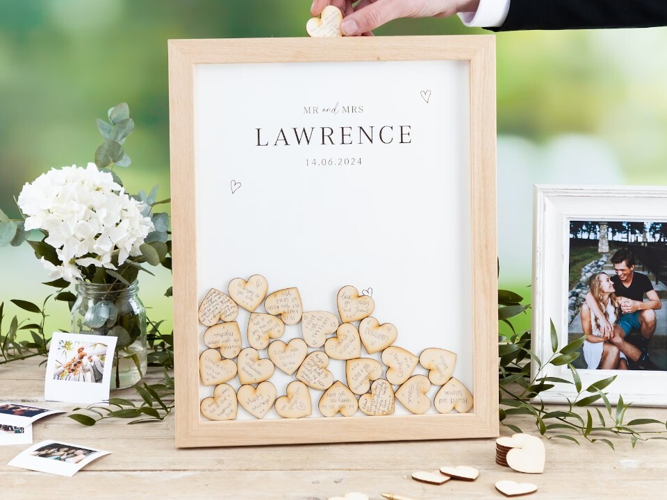 see through box framed with wooden hearts inserted inside with wedding guest signatures and phots of the couple surrounding the frame