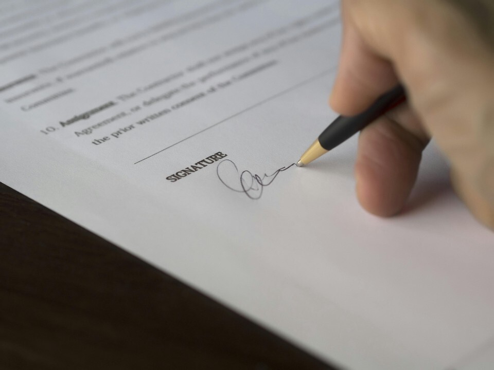 Hands holding a pen while signing a prenuptial agreement