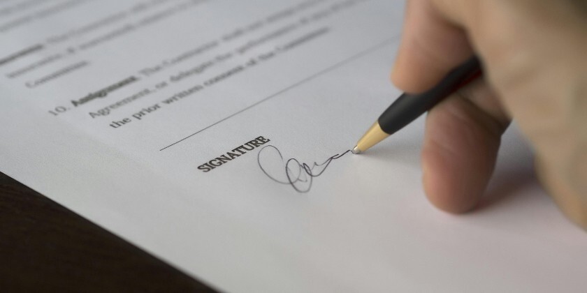 Hands holding a pen while signing a prenuptial agreement