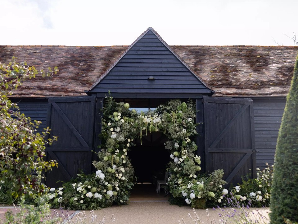 Alfriston Gardens Century Barn entrance decorated with elegant white and green wedding flowers in East Sussex.