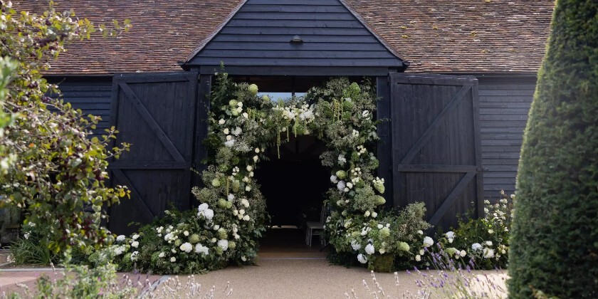 Alfriston Gardens Century Barn entrance decorated with elegant white and green wedding flowers in East Sussex.